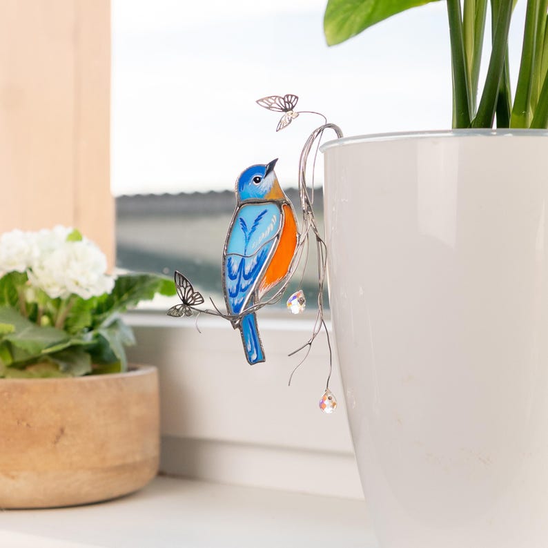 Radiant bluebird plant stake with glowing crystals and fluttering butterflies.