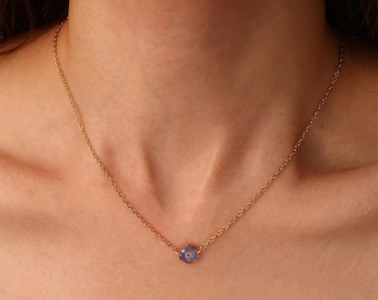 May include: A delicate gold-toned necklace featuring a small, light purple flower pendant. The chain is thin and hangs gracefully, showcasing the single floral accent. The necklace is a simple, elegant piece of jewelry.