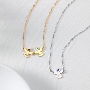 May include: Two necklaces with angel pendants. One is gold-toned, featuring two angels with purple and blue gemstones, and the names "Milo" and "Max". The other is silver-toned, with a single angel pendant and a blue gemstone, also with the name "Max".