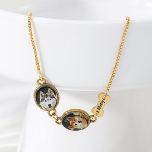 Könnte beinhalten: Ein goldfarbenes Kettenarmband mit zwei ovalen Anhängern mit Hundeporträts und einem kleinen knochenförmigen Anhänger, in den der Name Westley eingraviert ist. Das Armband hat ein feines Boxkettendesign und verbindet die Anhänger linear.