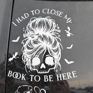Puede incluir: Calcomanía de vinilo blanco con un diseño de calavera con moño desordenado, rodeada de murciélagos. El texto dice "I HAD TO CLOSE MY BOOK TO BE HERE" y "Ohana".