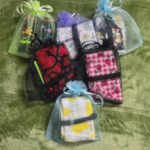 May include: A collection of small fabric items, each wrapped in a sheer mesh bag and tied with a ribbon. The fabrics feature various patterns, including hearts, cherries, lemons, and cartoon characters. The bags are in various colors.
