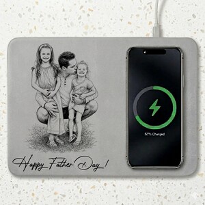 May include: A gray wireless charging pad with a pencil sketch of a father and two daughters. A smartphone is charging on the pad, displaying a green charging symbol and "57% Charged." The words "Happy Father Day!" are written in cursive.