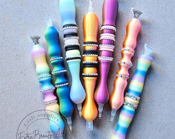 May include: A collection of colorful diamond painting pens. Each pen features a unique design with gradient colors, rhinestones, and a clear tip. The pens are labeled with the text "Craft Supplies Extra Beauty Art Mixed Media".