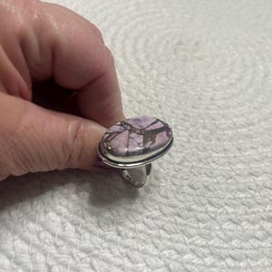 May include: Oval ring with a pink and brown patterned stone set in a silver band. The stone's design is a mix of pink and brown. This ring is a piece of jewellery.