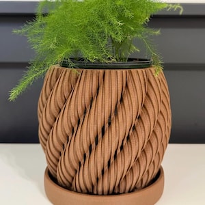 Peut inclure: Un pot de plante marron texturé, imprimé en 3D, avec un motif en spirale, contenant une plante verte vibrante. Le pot repose sur une soucoupe assortie, créant un look moderne pour les plantes d'intérieur.