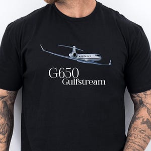 Puede incluir: Una camiseta negra de manga corta con un gráfico de un jet privado Gulfstream G650 blanco en vuelo. El texto G650 Gulfstream está impreso en letras blancas debajo del gráfico de la aeronave en la parte delantera de la camiseta.