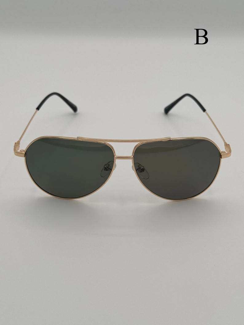 Puede incluir: Gafas de sol de aviador con montura dorada y lentes oscuras. Las gafas tienen un doble puente y patillas negras. La letra "B" es visible en la esquina superior derecha. Dise&ntilde;adas para protecci&oacute;n ocular y moda.