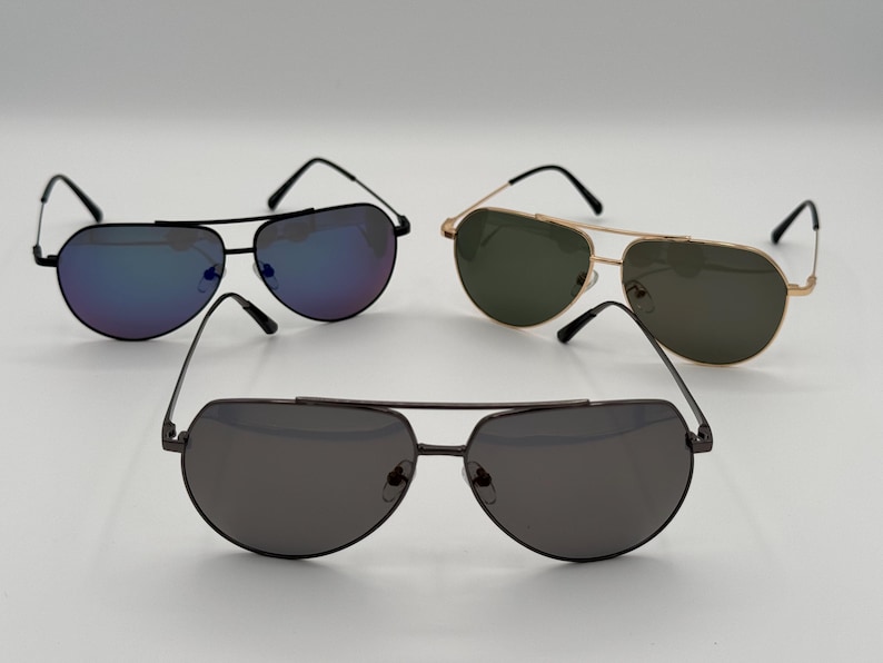 Puede incluir: Tres pares de gafas de sol de aviador con lentes de diferentes colores. Un par tiene monturas negras y lentes azul-p&uacute;rpura, otro tiene monturas doradas y lentes verdes, y el tercero tiene monturas gris oscuro y lentes grises.