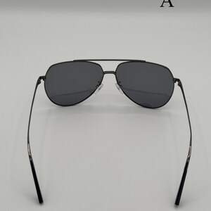Puede incluir: Gafas de sol de aviador negras con lentes oscuras y una fina montura met&aacute;lica. Las gafas tienen un doble puente y una forma cl&aacute;sica de l&aacute;grima. Las patillas son delgadas y se extienden hacia los extremos. La letra "A" es visible en el fondo.