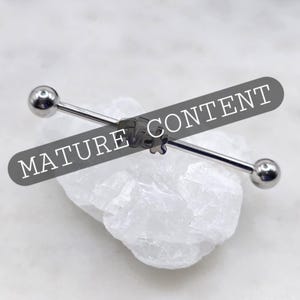 May include: A silver industrial barbell earring with a small flower design in the center. The barbell has a ball on each end. The text "MATURE CONTENT" is across the image.