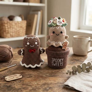 May include: Two crocheted gingerbread figures. One is a standalone gingerbread person with a red bow tie and white icing trim. The other is a ghost-like figure wearing a floral crown, sitting atop a brown pot labeled with the text SPOOKY SWEETS.