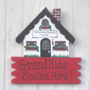 May include: A white wooden house with a black roof and red chimney. The house has a sign that says "Grandma & Grandpa's House". Below the house is a red sign that says "Grand Kids Spoiled Here!"
