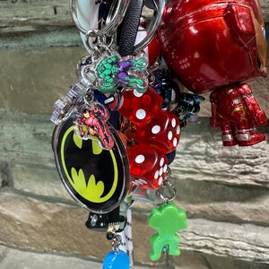 May include: A collection of keyrings with various designs. Includes a red Iron Man figure, Batman logo, Hulk, and red dice. Other keyrings have a blue, green, and white colour scheme. The keyrings are attached to silver keyrings.