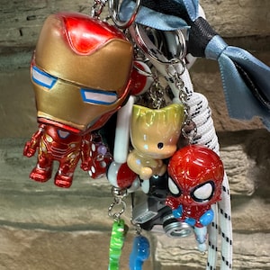 May include: A selection of superhero keyrings featuring Iron Man, Spider-Man, and Baby Groot characters, plus other colourful charms. The keyrings are attached to metal rings and a lanyard with a blue ribbon.