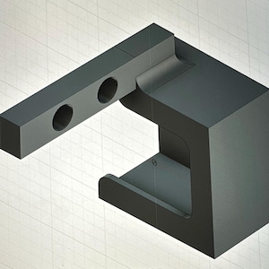 Può includere: Oggetto geometrico grigio scuro, renderizzato in 3D, con una base rettangolare e un braccio esteso con due fori circolari. Il design include un'indentazione curva e una sezione ritagliata, su uno sfondo a griglia.