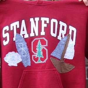 May include: A red hooded sweatshirt with the word "STANFORD" in white block letters across the chest. Below the text is a large "S" with a tree inside, and sailboat and seashell appliqués.