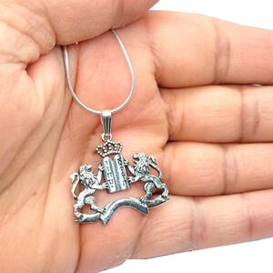 May include: A silver necklace with a pendant featuring two lions holding a crown and a scroll with Hebrew text. The pendant is a stylized representation of the Coat of Arms of Israel.
