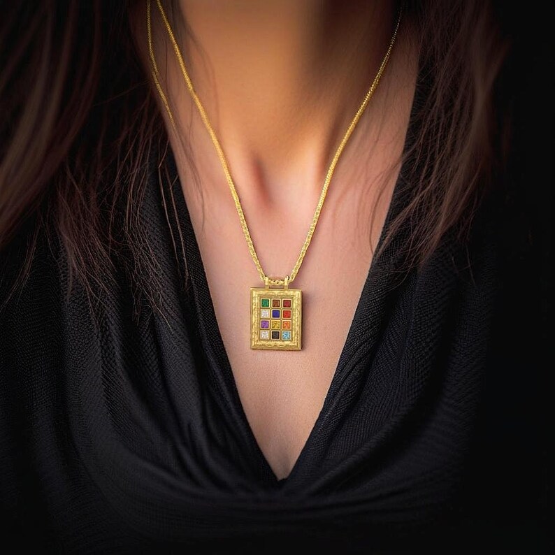 Pu&ograve; includere: Una collana con catena d'oro con un ciondolo quadrato che presenta una griglia di pietre preziose colorate. Il ciondolo &egrave; ornato e ha un bordo dettagliato.