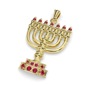 Könnte beinhalten: Ein goldener Menora-Anhänger mit roten Edelsteinen. Die Menora hat sieben Arme und eine Basis mit einem dekorativen Design.