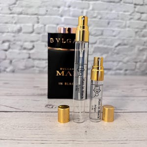 Pode incluir: Dois pequenos frascos de perfume de vidro com tampas douradas e etiquetas que dizem "Man in Black" e "Bvlgari".