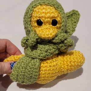 May include: A crocheted yellow duck wearing a green crocheted scarf and hood.
