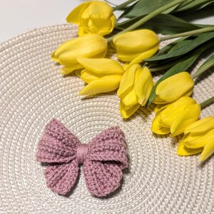 May include: A pink crocheted bow on a woven placemat with yellow tulips in the background.