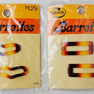 May include: Two sealed plastic packages of Goody barrettes. The left package contains two chevron-shaped hair clips, and the right package contains two rectangular hair clips. All four clips feature a brown, black, and yellow tortoiseshell pattern.