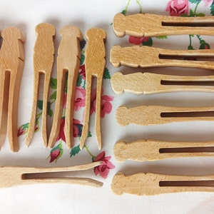 May include: A collection of wooden clothespins, featuring a light brown color and a classic design. The clothespins are arranged on a floral patterned fabric, showcasing their traditional form and functionality. These are ideal for laundry or craft projects.