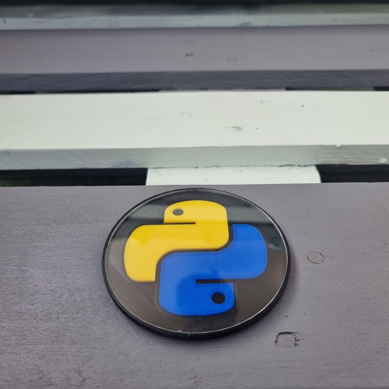 May include: A black and white round sticker with a yellow and blue Python logo. The logo is a stylized snake with a yellow body and a blue tail.