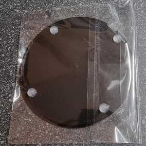 May include: A black round coaster with four white rubber feet on the bottom. The coaster is packaged in a clear plastic bag.