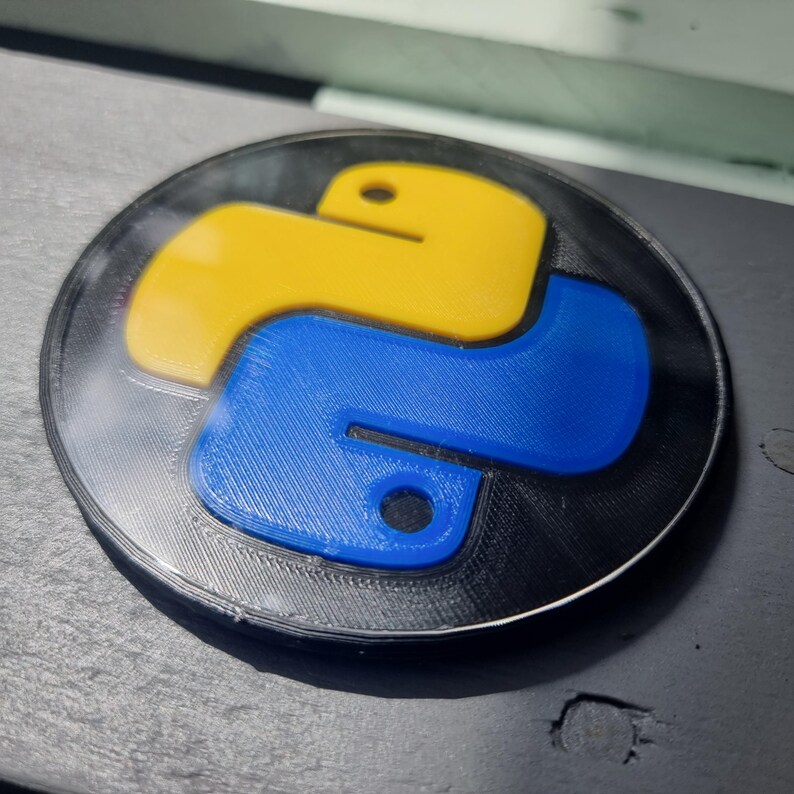 May include: A 3D printed Python logo keychain with a black background, a yellow top, and a blue bottom.