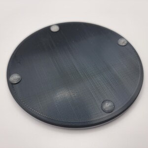 May include: A round, black, plastic coaster with four small, clear, rubber feet on the bottom.