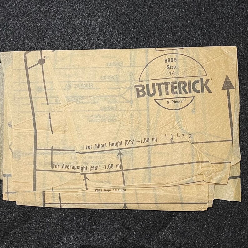 May include: A vintage sewing pattern for a garment, labelled "Butterick" with pattern number 6899 and size 14. The pattern includes 9 pieces and instructions for short and average height.