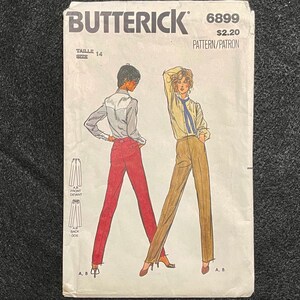 May include: A vintage sewing pattern for trousers, size 14, from Butterick pattern number 6899. The pattern is for a pair of trousers with a wide leg and a high waist. The pattern is illustrated with two figures wearing the trousers, one in red and one in brown.