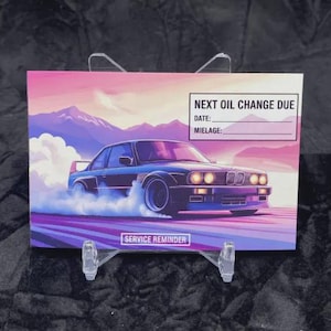 May include: A service reminder card featuring a blue car drifting on a purple and pink track, with mountains in the background. The card has text that reads "NEXT OIL CHANGE DUE" and "SERVICE REMINDER".