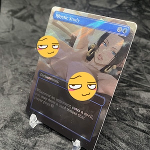 Pode incluir: Uma carta colecionável retangular intitulada Rhystic Study com um cabeçalho azul contendo o texto Rhystic Study e um símbolo de custo de mana. A carta exibe a ilustração de um personagem de cabelo escuro e brincos dourados, parcialmente oculto por dois adesivos de emoji amarelos.