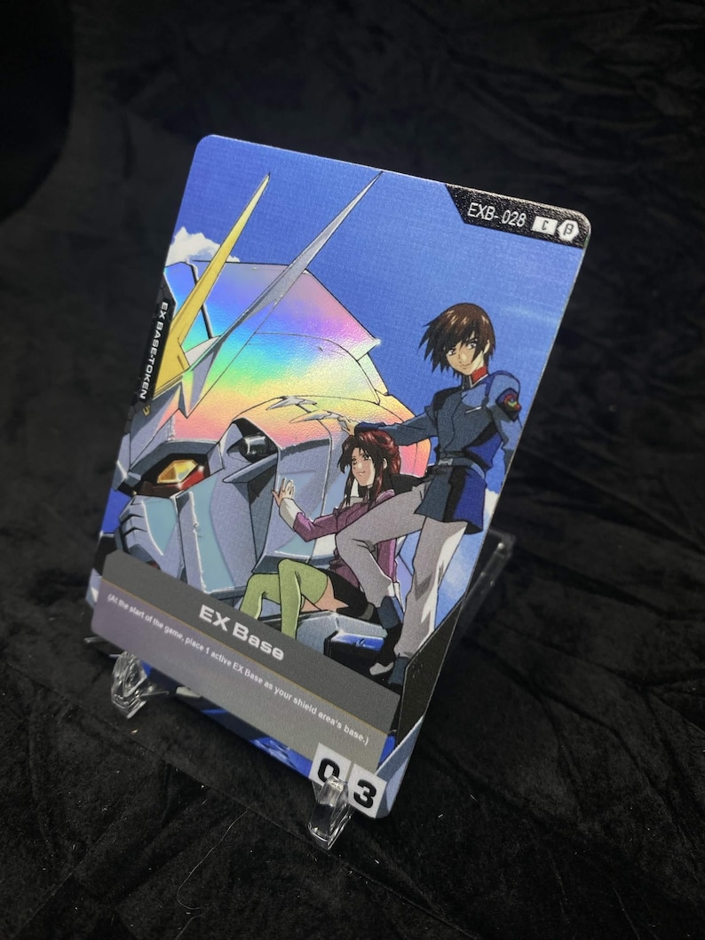 May include: A holographic trading card featuring anime characters and a robot. The card has the text "EX Base" and "EXB-028". The background is blue with a futuristic design. The card is displayed on a clear stand.