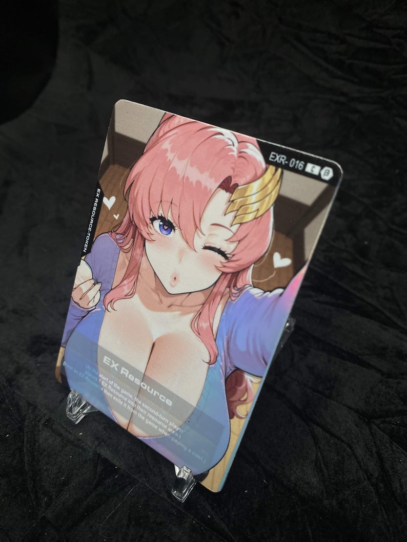 Puede incluir: Una tarjeta coleccionable con una ilustraci&oacute;n de estilo anime de una mujer con cabello rosado, ojos azules y una pieza de cabeza dorada. La tarjeta est&aacute; etiquetada como "EX Resource" y "EXR-016 B". La tarjeta se muestra en un soporte de pl&aacute;stico transparente.