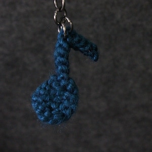 Könnte beinhalten: Ein blauer gehäkelter Musiknotenschlüsselanhänger mit einer silbernen Metallkette.