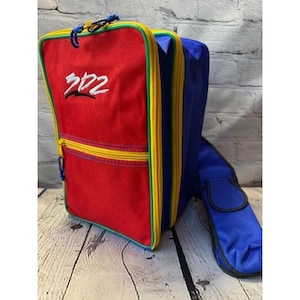May include: A colorful backpack with a red front panel featuring the embroidered text "202". The backpack has a yellow zipper, blue and yellow trim, and a blue extension. The design is completed with a blue and yellow drawstring.