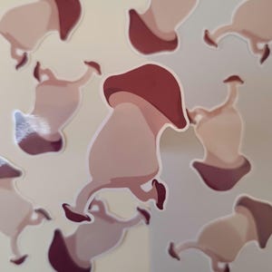 May include: A collection of stickers featuring a cartoon mushroom design. The mushrooms have a light pink body and a dark burgundy cap. The stickers are scattered across a light beige background.