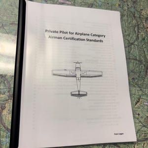 May include: A black and white illustration of a single-engine airplane on a white page with the text "Private Pilot for Airplane Category Airman Certification Standards" and "Evan Logan" at the bottom.
