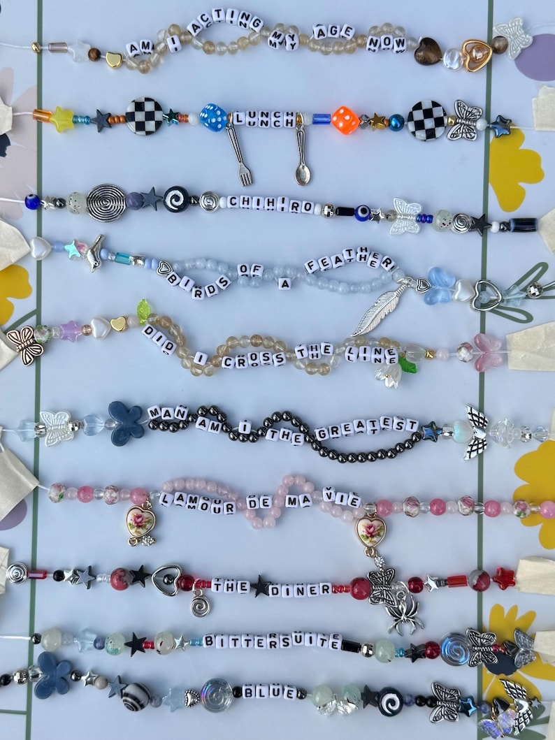 Pu&ograve; includere: Una collezione di braccialetti di perline con vari disegni e testo. I braccialetti presentano perline colorate, ciondoli e parole come "Acting My Age Now", "Lunch" e "Chihir0". Alcuni braccialetti hanno ciondoli a forma di farfalla e stella.