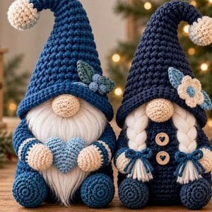 May include: Two crocheted gnomes with blue pointed hats topped with cream pom-poms. The left gnome has a white beard and holds a light blue heart. The right gnome features white braided hair, two wooden heart buttons, and a cream flower on its hat.