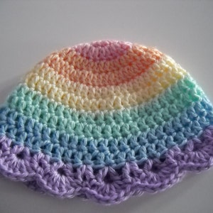 Puede incluir: Un gorro de ganchillo con un patr&oacute;n de degradado de arco&iacute;ris en tonos pastel. El dise&ntilde;o transita desde un rosa suave en la coronilla pasando por amarillo, verde menta y azul claro, con un borde festoneado morado en la parte inferior.