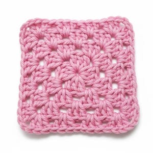 May include: A square crochet granny square motif made with thick, light pink yarn. The design features a central cluster of stitches radiating outward into a geometric pattern with open spaces between the yarn loops, creating a textured, handmade textile.