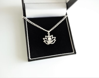 May include: A silver-colored necklace with a lotus flower pendant, presented in a black jewelry box. The pendant features a seated figure in a lotus position within the flower's petals. The chain is a curb style.