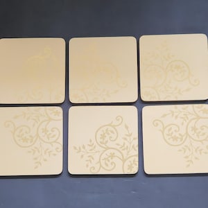 Peut inclure: Un ensemble de six dessous de verre carrés de couleur beige clair, chacun présentant un motif floral délicat et tonal en forme de vigne qui s'incurve depuis le coin sur la surface. Les dessous de verre sont disposés en deux rangées de trois.