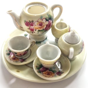 Puede incluir: Un juego de té en miniatura de porcelana que incluye una tetera, una lechera, un azucarero con tapa y dos tazas con sus platos a juego, dispuestos sobre una bandeja redonda. Cada pieza presenta un diseño floral de rosas amarillas y rosas.